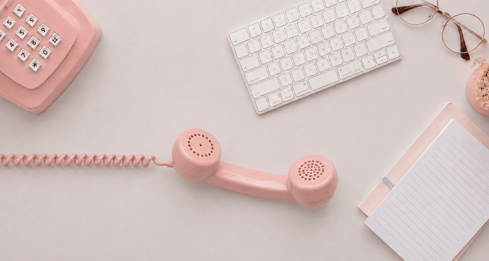 Rosa Telefon mit abgenommenem Hörer neben Tastatur und Notizblock auf hellem Schreibtisch